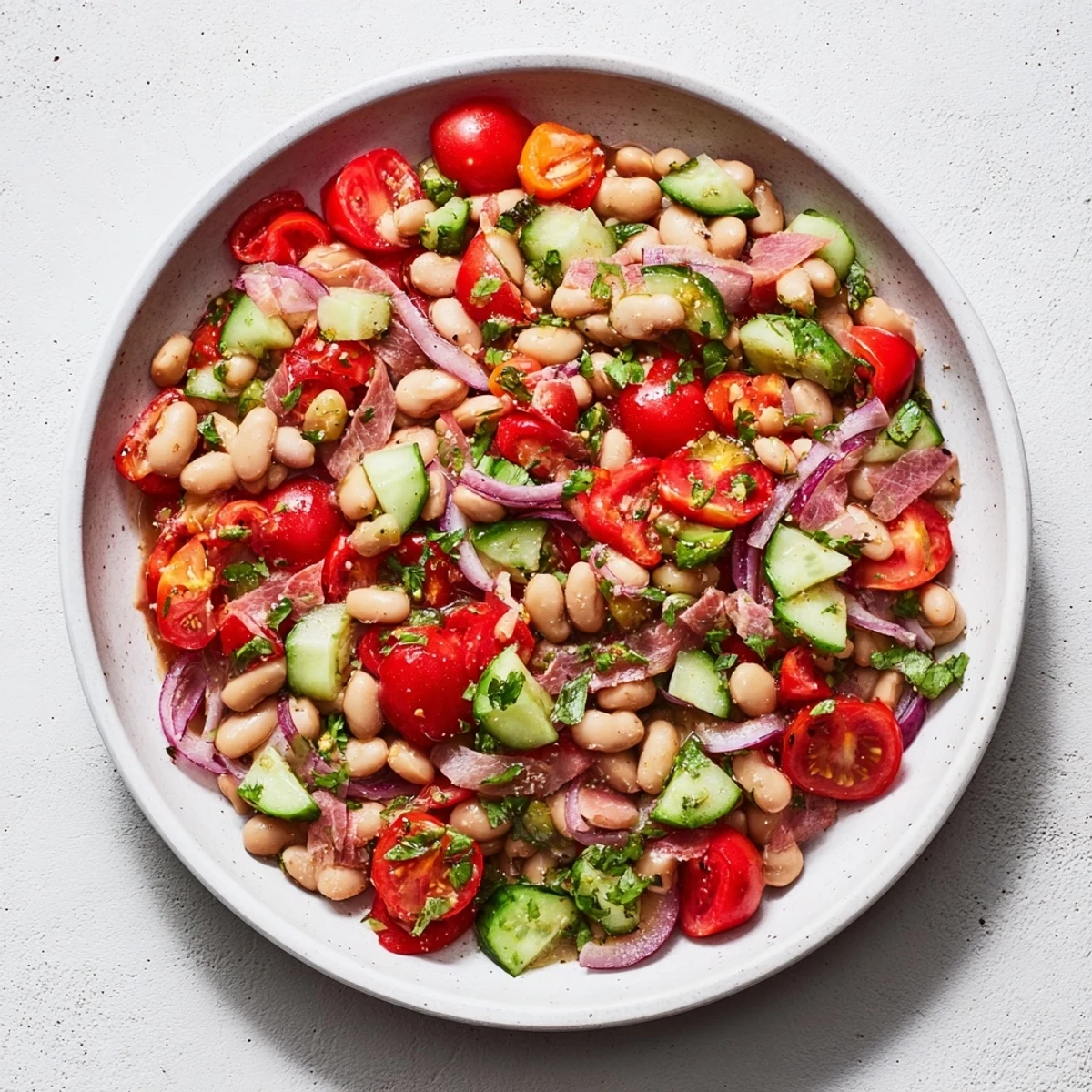 Close-up of vibrant Dense Bean Salad with prosciutto, garnished with fresh herbs and colorful vegetables.