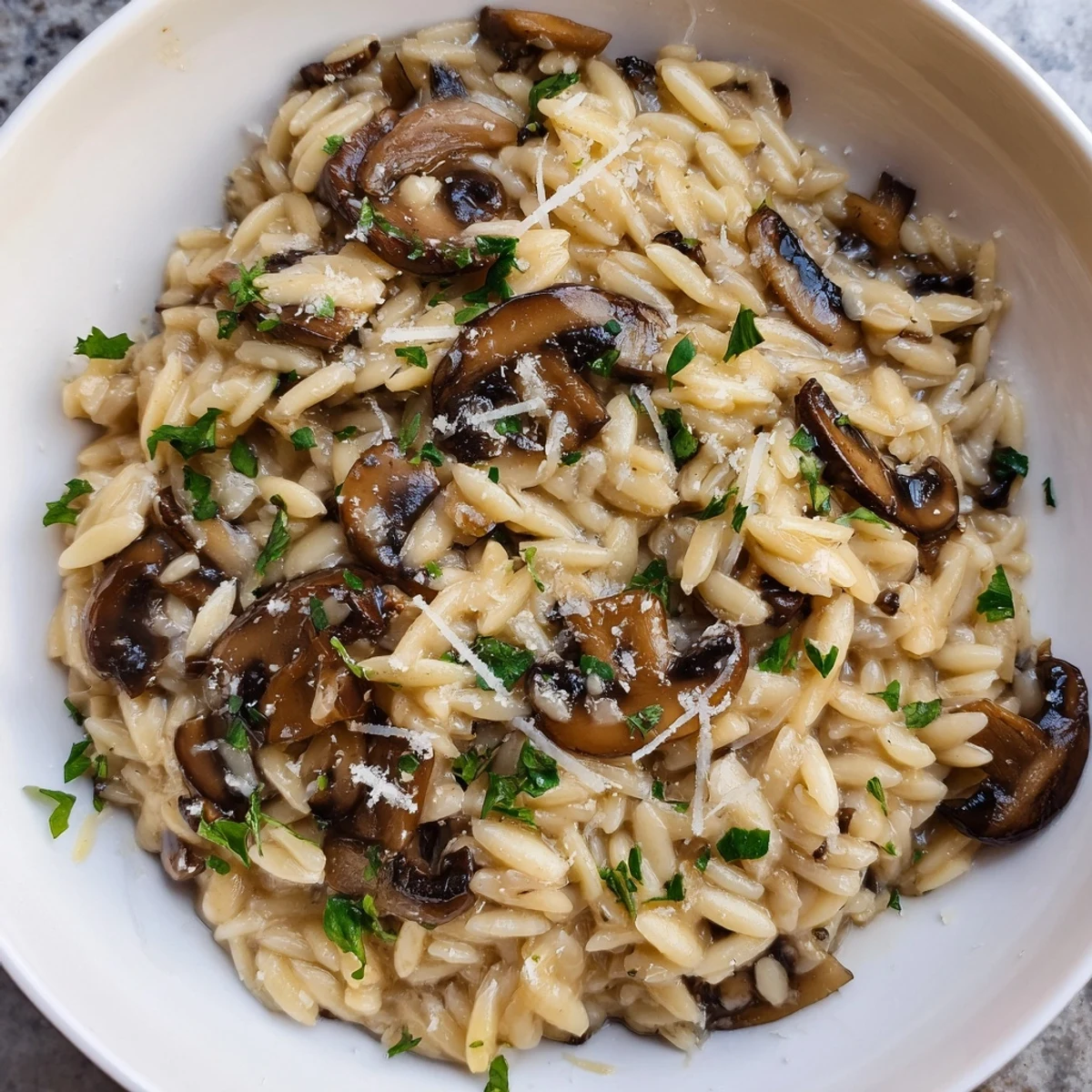 Steaming bowl of orzo mushroom risotto-style, showcasing the creamy texture and mushroom slices.
