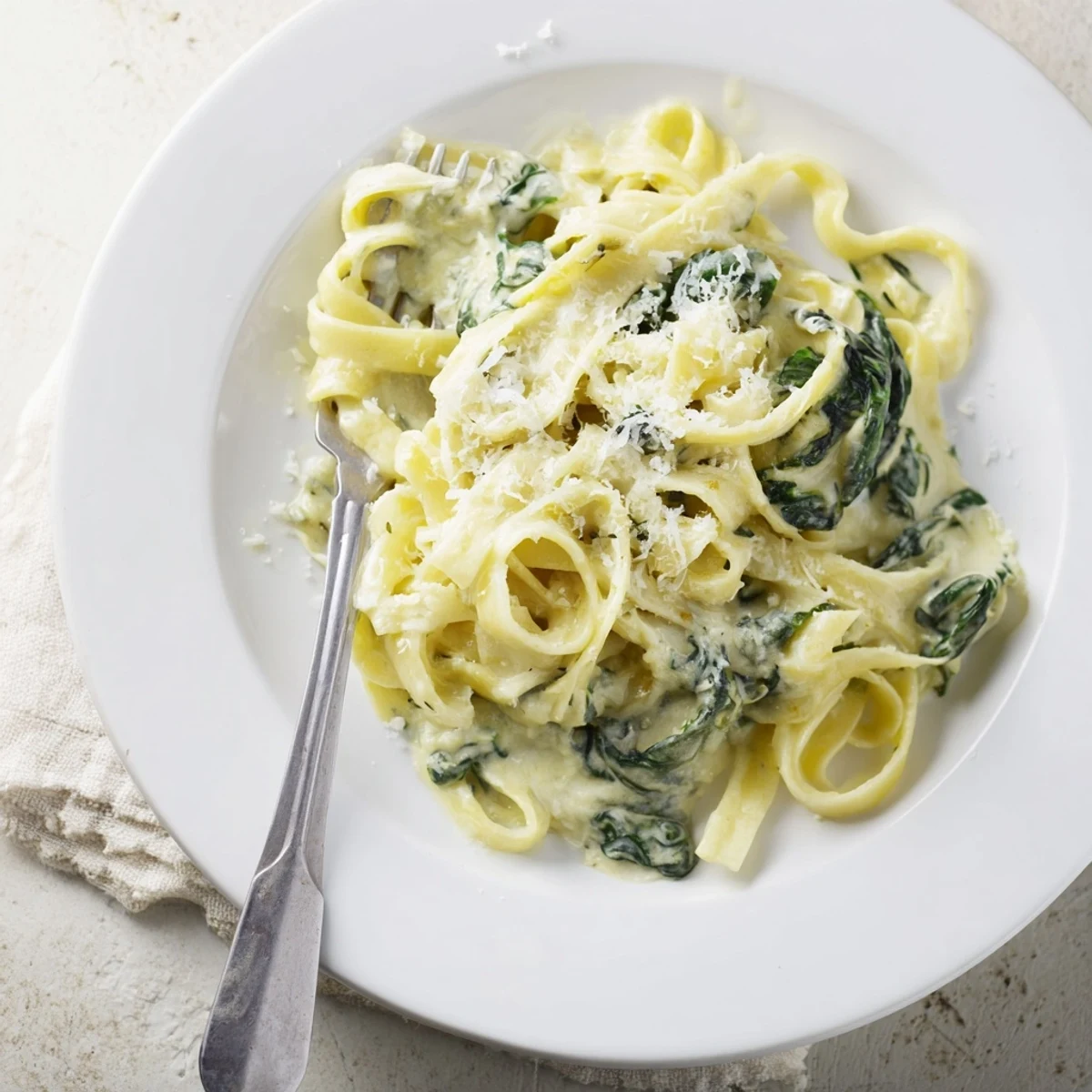 A close-up of Creamy Spinach Garlic Noodles, with steam rising from a creamy, golden sauce flecked with fresh spinach and garlic.