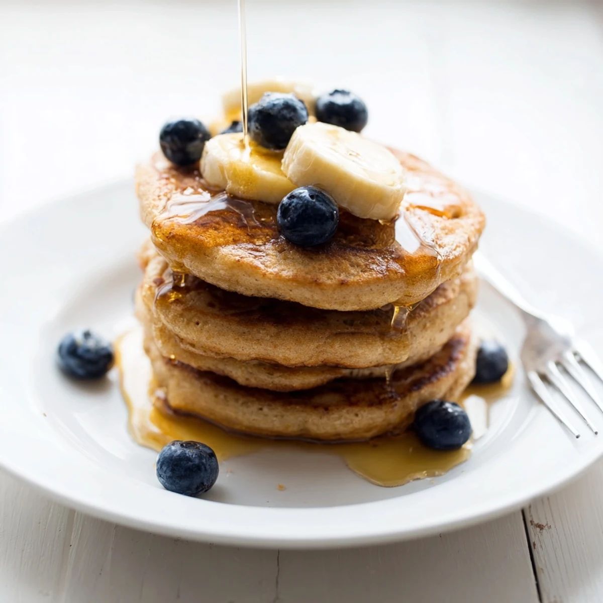 A fork lifts a bite of Protein Power Pancakes, revealing a tender, airy interior and a generous dollop of Greek yogurt.