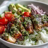 Colorful chimichurri chicken bowl features zesty herb-marinated chicken, cherry tomatoes, and a drizzle of vibrant green sauce.