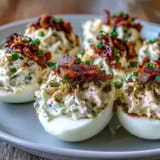 Deviled eggs filled with bacon and ranch dressing, topped with crunchy bacon bits and a sprinkle of paprika for extra flavor.