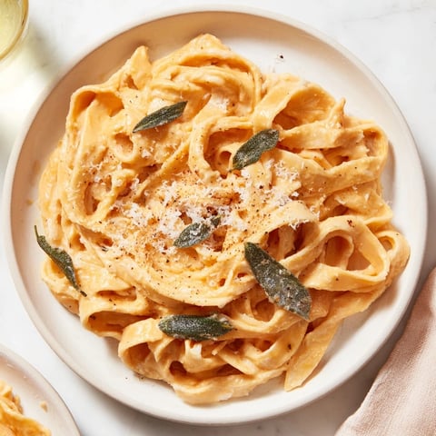 A photo shows a vibrant bowl of Healthy Creamy Pumpkin Sage Holiday Pasta, garnished with fresh herbs.