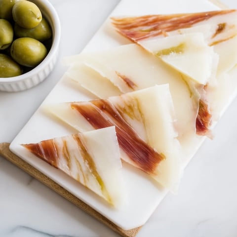 Elegant Minimalism Master cheese board featuring aged Comté, Jamón Ibérico, and bright green olives.