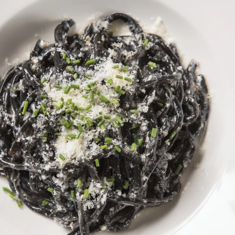 Silky Squid Ink Pasta with creamy sauce, Parmesan, and chives, ready to serve and enjoy.