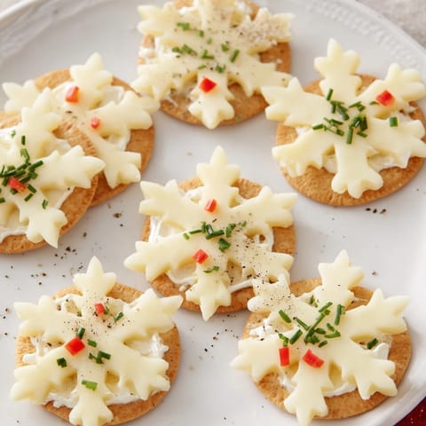 Elegant Cracker and Cheese Snowflake Bites boast a delicate snowflake design atop crispy crackers, perfect party food.