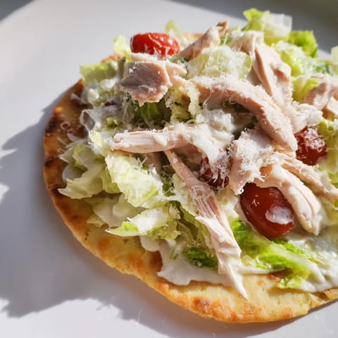 A close-up of Caesar Chicken Flatbread topped with juicy chicken, crisp lettuce, and cherry tomatoes beside a lemon wedge.  