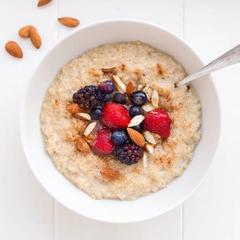 Steaming hot Millet Porridge With Berries in a rustic ceramic bowl, garnished with sliced almonds and a maple drizzle.