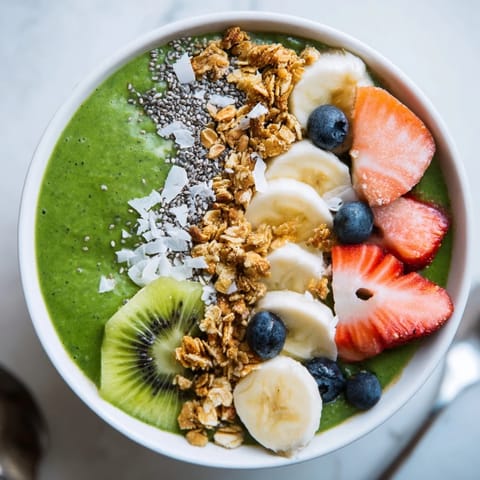 Close-up of a creamy Green Smoothie Bowl with sliced bananas, blueberries, and a drizzle of honey on top.