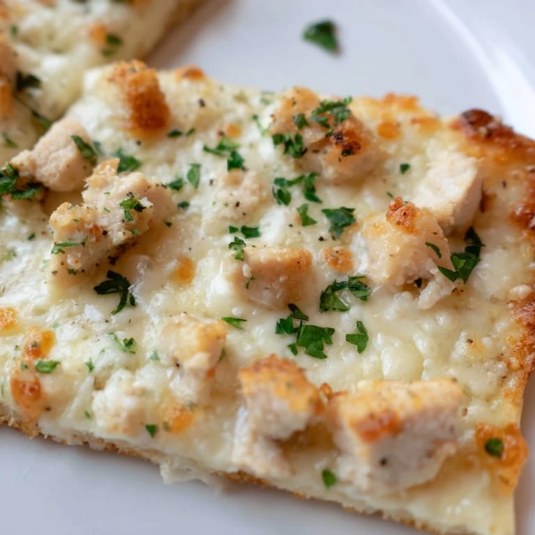 Close-up of Chicken Alfredo Pizza with creamy white sauce, melted mozzarella, and parsley garnish.